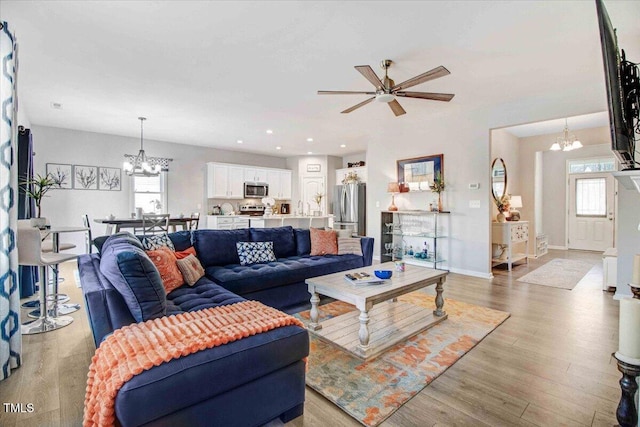 living room with ceiling fan with notable chandelier and light hardwood / wood-style flooring