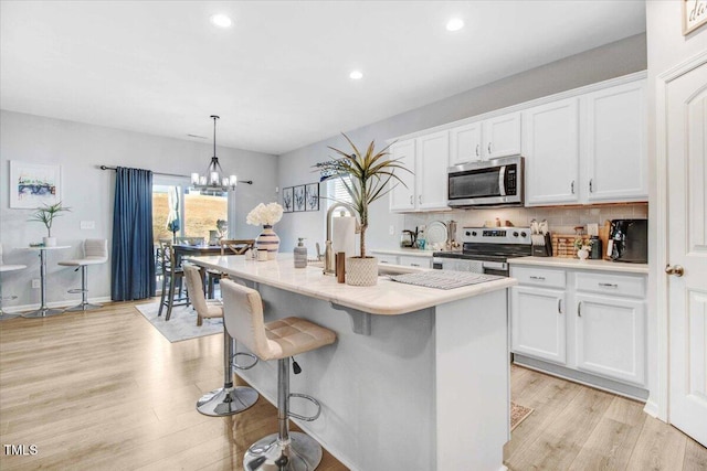 kitchen with white cabinetry, a center island with sink, appliances with stainless steel finishes, decorative light fixtures, and light wood-type flooring