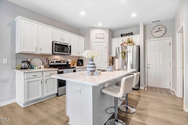 kitchen with white cabinets, appliances with stainless steel finishes, sink, and a center island with sink