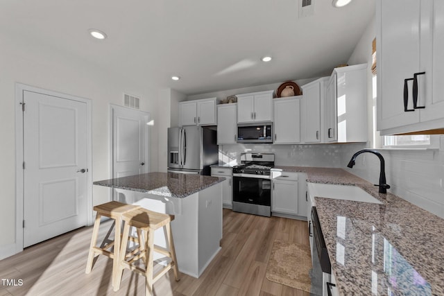 kitchen featuring a breakfast bar, white cabinetry, a center island, stainless steel appliances, and light stone countertops