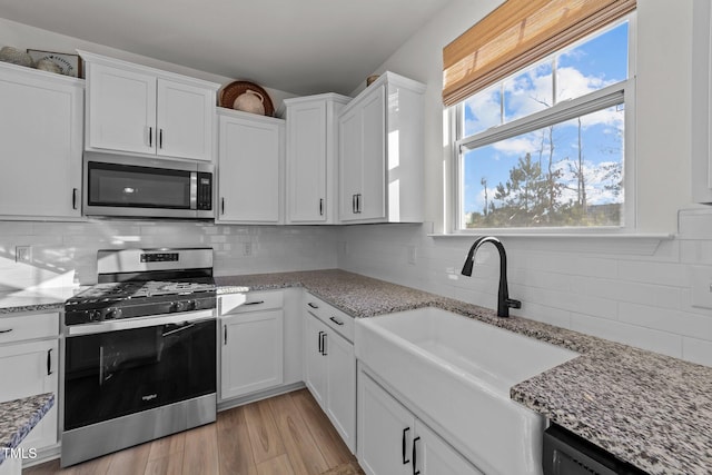 kitchen with white cabinetry, appliances with stainless steel finishes, sink, and light stone counters