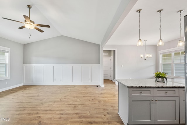 kitchen with pendant lighting, light stone counters, gray cabinets, light hardwood / wood-style floors, and lofted ceiling