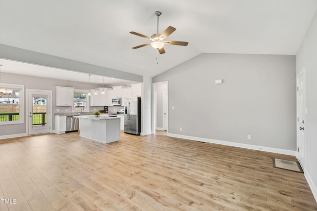 unfurnished living room with vaulted ceiling, ceiling fan with notable chandelier, and light hardwood / wood-style flooring