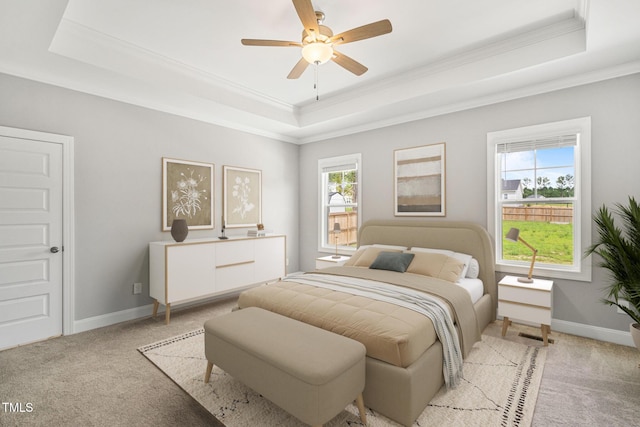 bedroom with ceiling fan, light carpet, multiple windows, and a tray ceiling