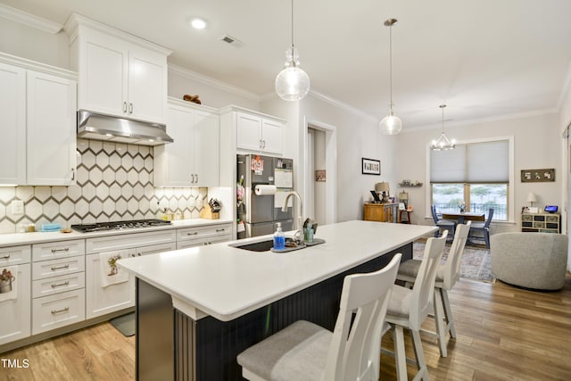 kitchen featuring appliances with stainless steel finishes, white cabinetry, pendant lighting, an island with sink, and backsplash