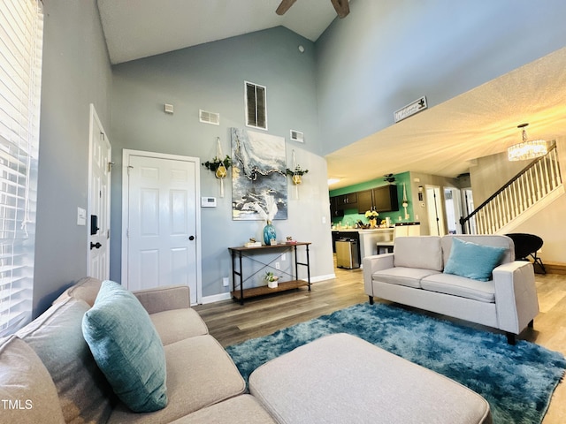 living room with ceiling fan with notable chandelier, high vaulted ceiling, and light hardwood / wood-style flooring