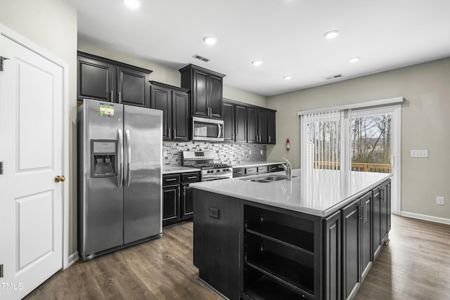 kitchen with sink, dark wood-type flooring, appliances with stainless steel finishes, an island with sink, and decorative backsplash