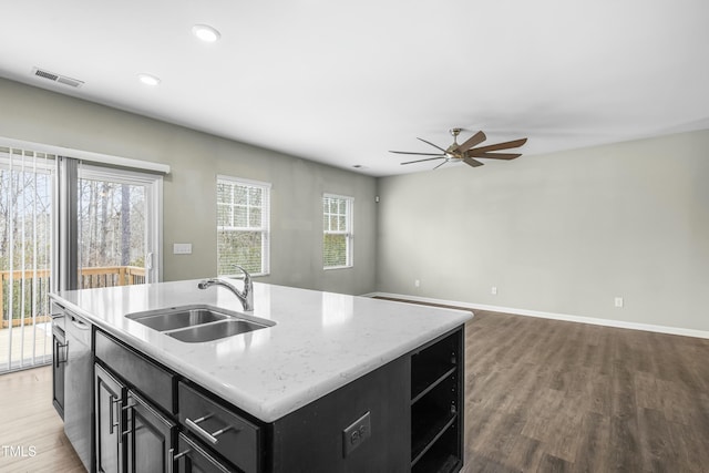 kitchen featuring sink, light stone counters, a center island with sink, stainless steel dishwasher, and hardwood / wood-style flooring