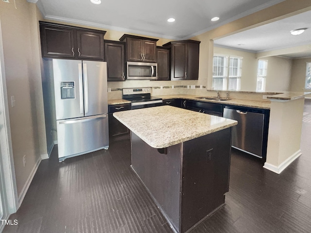 kitchen with a kitchen bar, appliances with stainless steel finishes, sink, a kitchen island, and ornamental molding