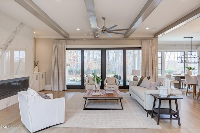 living room with ceiling fan with notable chandelier, beamed ceiling, and light wood-type flooring