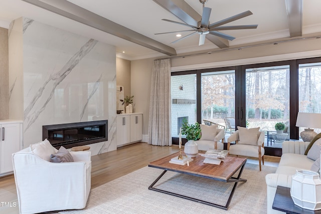 living room featuring beamed ceiling, ceiling fan, a fireplace, and light hardwood / wood-style flooring