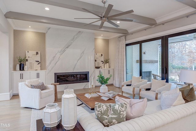 living room featuring beamed ceiling, a premium fireplace, crown molding, and light wood-type flooring