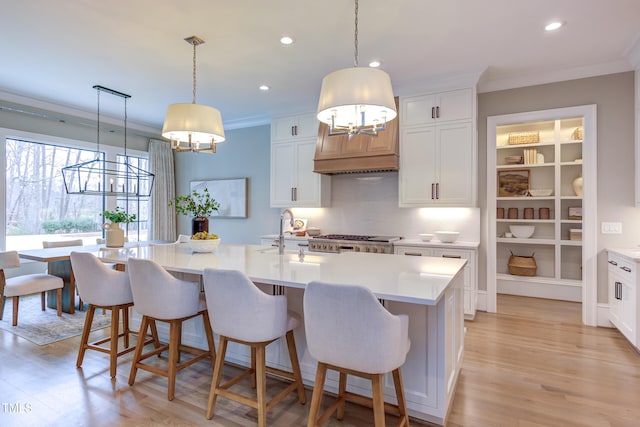 kitchen with ornamental molding, a center island with sink, white cabinets, and decorative light fixtures