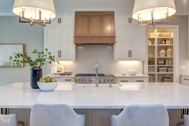 kitchen featuring a notable chandelier, decorative light fixtures, white cabinets, and a center island with sink