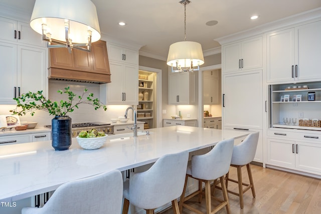 kitchen featuring pendant lighting, white cabinets, ornamental molding, light stone counters, and light wood-type flooring