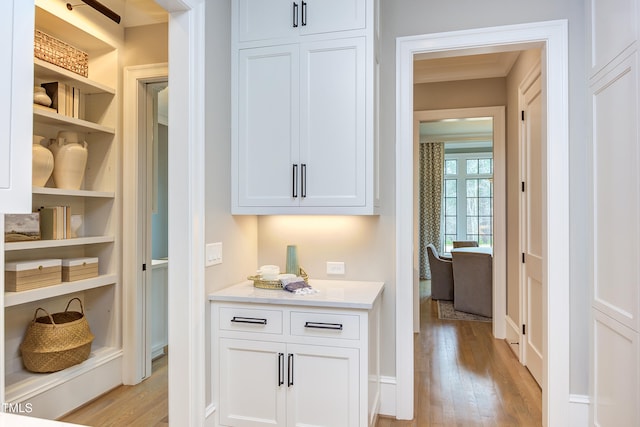 interior space with ornamental molding, white cabinets, built in features, and light hardwood / wood-style flooring