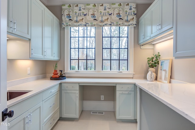 kitchen featuring light stone counters, built in desk, a healthy amount of sunlight, and light tile patterned flooring