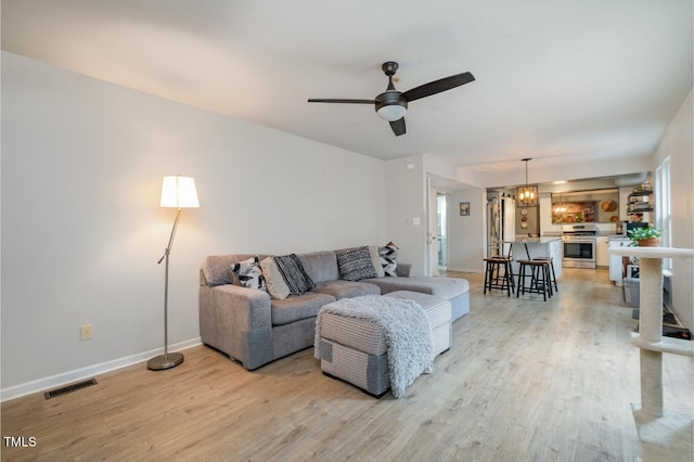 living room featuring ceiling fan with notable chandelier and light hardwood / wood-style flooring