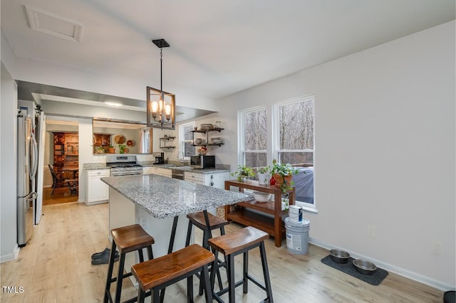 kitchen featuring a breakfast bar, white cabinetry, stainless steel appliances, light stone counters, and light hardwood / wood-style floors