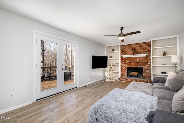 living room with french doors, ceiling fan, a fireplace, and light hardwood / wood-style flooring