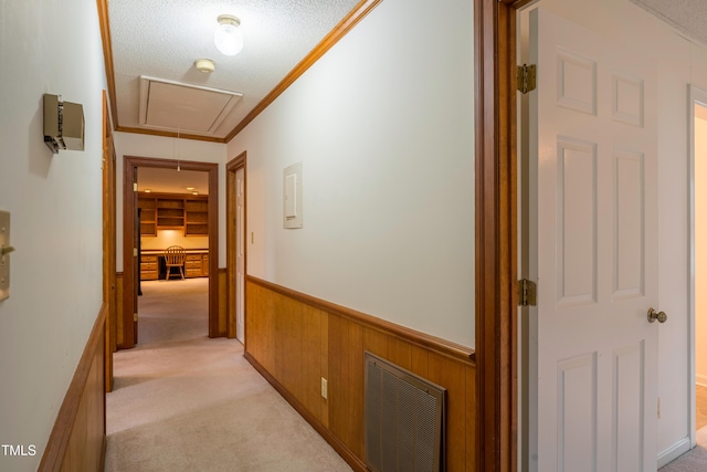 hallway with light carpet, ornamental molding, a textured ceiling, and wood walls