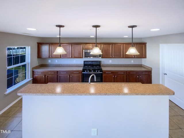 kitchen featuring black range with gas stovetop, a kitchen island with sink, light tile patterned floors, and pendant lighting