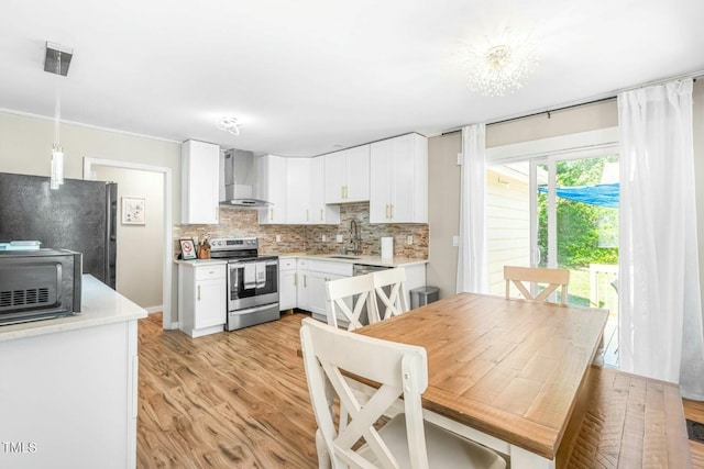 kitchen featuring wall chimney exhaust hood, sink, decorative light fixtures, white cabinets, and black appliances