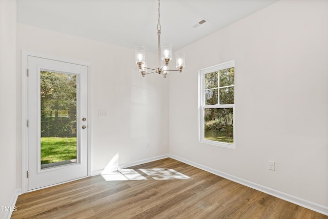 unfurnished dining area with wood-type flooring and a notable chandelier