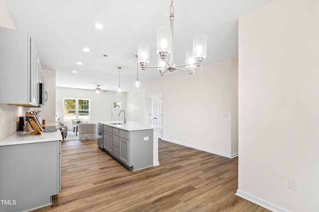 kitchen featuring pendant lighting, hardwood / wood-style flooring, gray cabinetry, stainless steel appliances, and a center island with sink