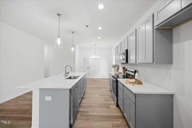 kitchen featuring gray cabinets, appliances with stainless steel finishes, an island with sink, sink, and hanging light fixtures