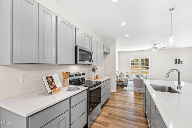 kitchen featuring pendant lighting, sink, gray cabinetry, stainless steel appliances, and light stone countertops