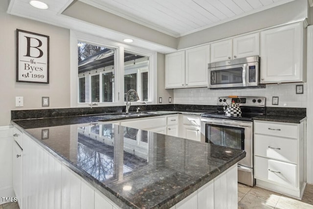 kitchen featuring dark stone countertops, ornamental molding, stainless steel appliances, decorative backsplash, and white cabinets