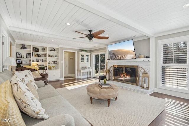 living room with beamed ceiling, built in features, a brick fireplace, and hardwood / wood-style flooring