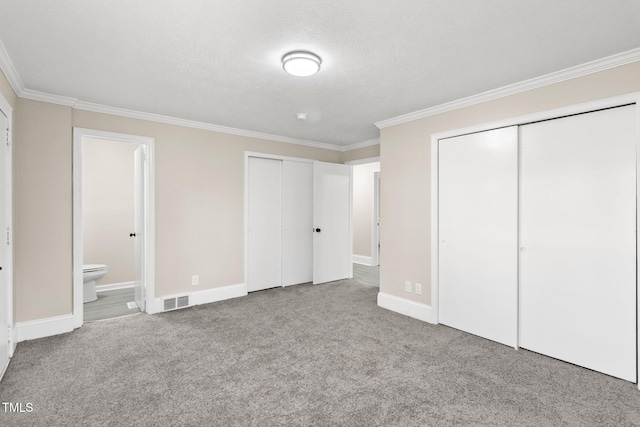 unfurnished bedroom featuring two closets, connected bathroom, ornamental molding, and light colored carpet