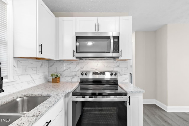 kitchen with a textured ceiling, white cabinets, stainless steel appliances, backsplash, and light stone counters