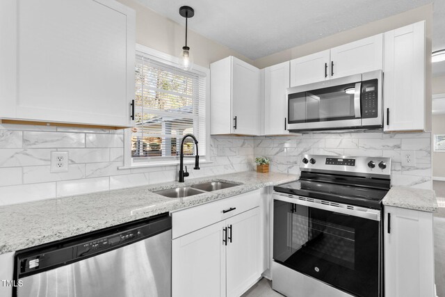 kitchen with appliances with stainless steel finishes, white cabinetry, sink, backsplash, and light stone counters