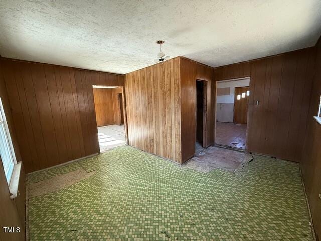 unfurnished room with a textured ceiling and wood walls