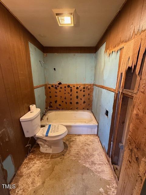 bathroom featuring wooden walls, toilet, and a tub to relax in