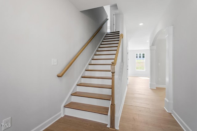 stairway featuring arched walkways, wood finished floors, baseboards, and recessed lighting