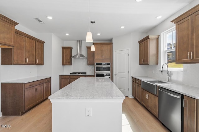 kitchen featuring wall chimney range hood, light wood-type flooring, appliances with stainless steel finishes, visible vents, and a kitchen island