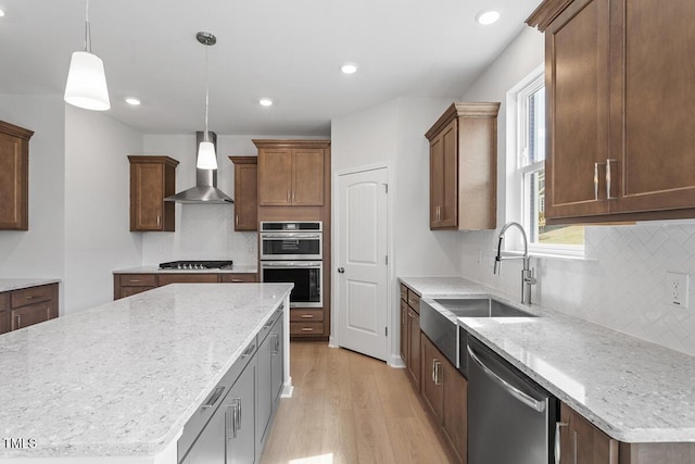 kitchen with a sink, light wood-style floors, wall chimney exhaust hood, tasteful backsplash, and appliances with stainless steel finishes