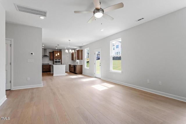 unfurnished living room with light wood-type flooring, baseboards, visible vents, recessed lighting, and ceiling fan with notable chandelier