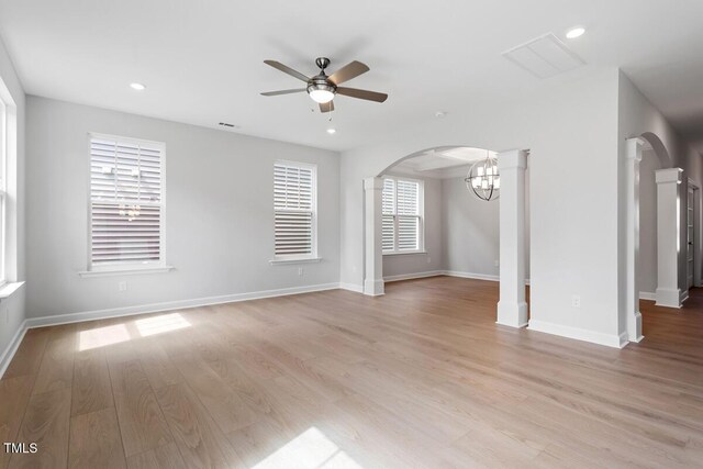 unfurnished living room with arched walkways, light wood-style floors, baseboards, and ceiling fan with notable chandelier