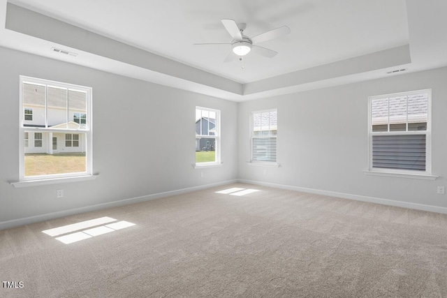 carpeted spare room with baseboards, a ceiling fan, a tray ceiling, and visible vents