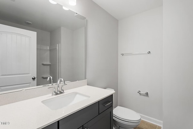 bathroom with toilet, vanity, a shower, and baseboards