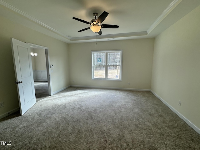 carpeted empty room featuring a ceiling fan, baseboards, a tray ceiling, and crown molding