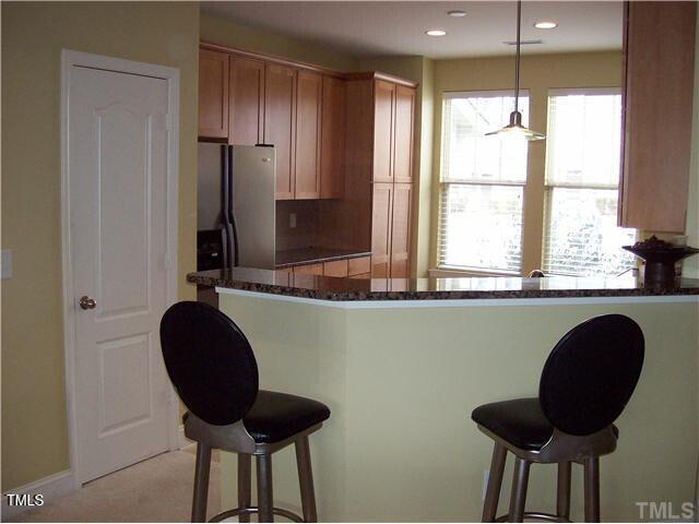 kitchen with kitchen peninsula, stainless steel refrigerator with ice dispenser, dark stone countertops, and pendant lighting