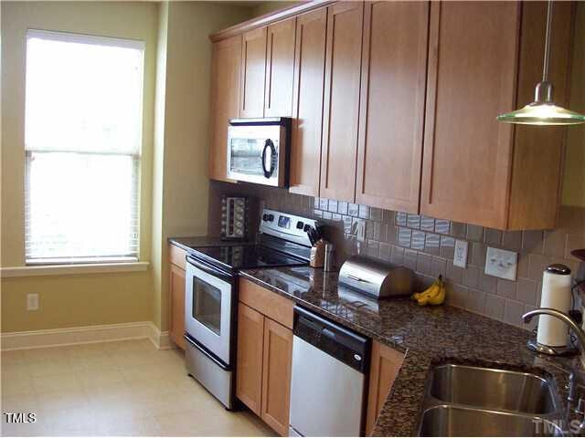 kitchen with appliances with stainless steel finishes, decorative light fixtures, dark stone countertops, sink, and backsplash