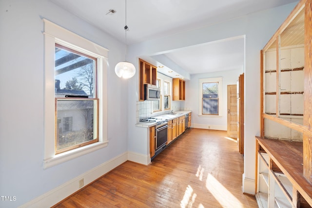 kitchen with sink, tasteful backsplash, decorative light fixtures, stainless steel appliances, and light hardwood / wood-style floors