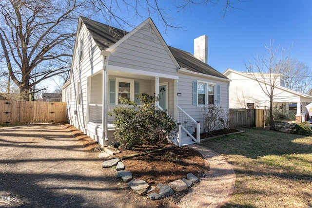 bungalow-style home featuring covered porch, a front lawn, a chimney, and fence